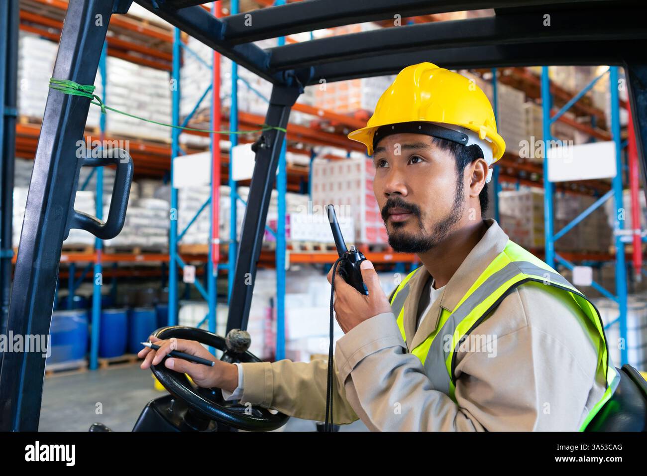 Lagerarbeiter in Sicherheitsausrüstung, der Gabelstapler bedient und über Funk, Kopierraum kommuniziert Stockfoto