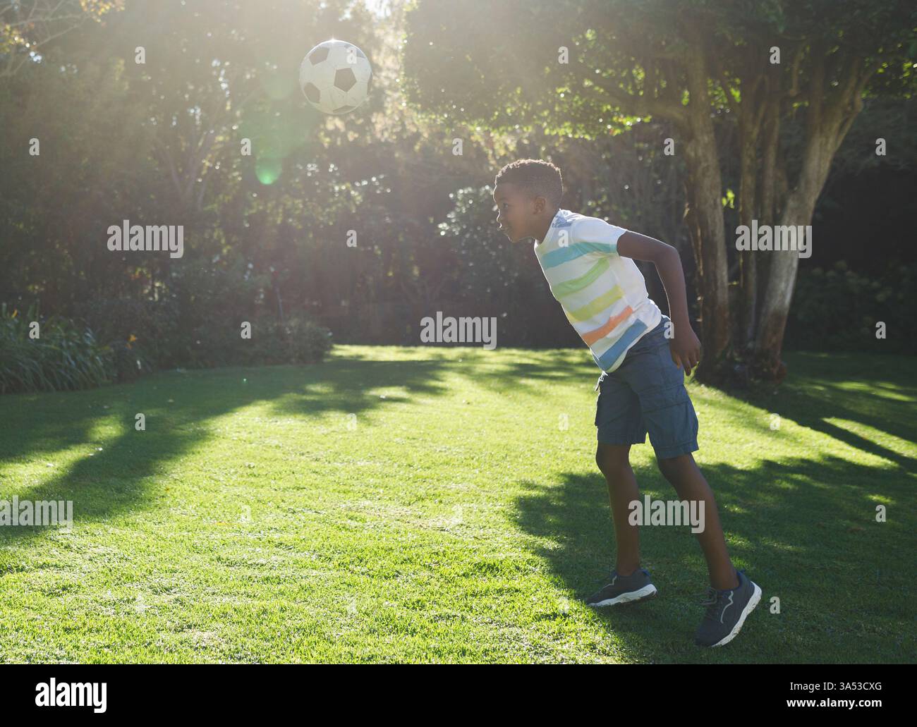Afroamerikanischer Junge, der im Hinterhof Fußball spielt, konzentriert sich auf den Heading Ball Stockfoto