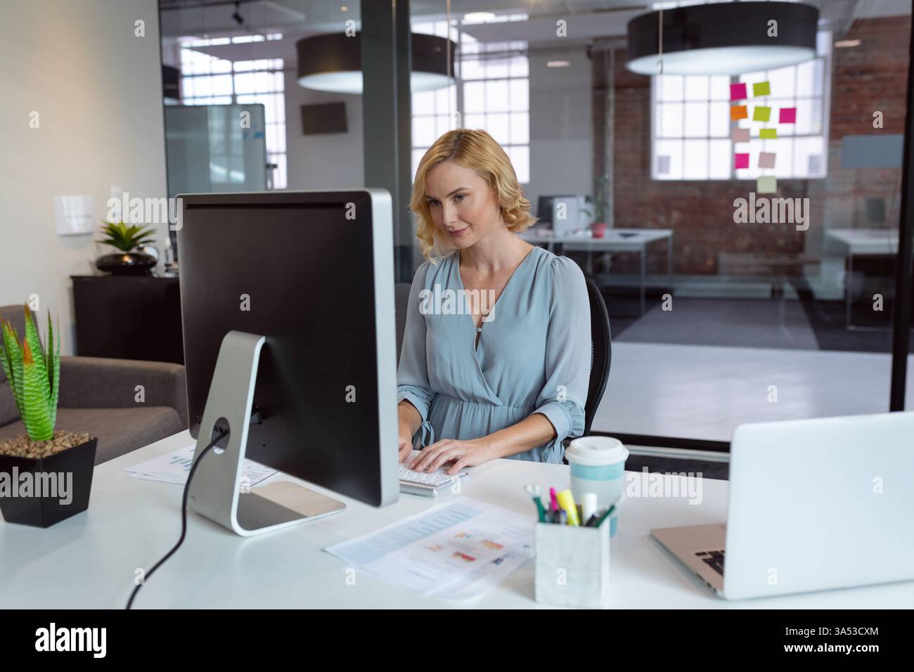 Professionelle Frau, die am Schreibtisch am Computer schreibt, konzentriert und produktiv Stockfoto
