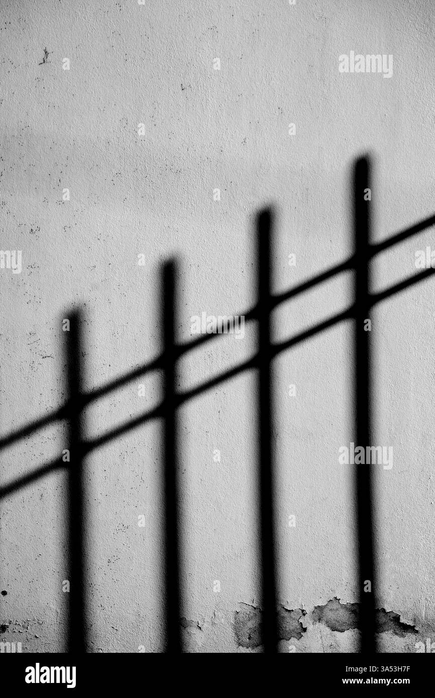 Die dunklen surrealen Schatten eines eisernen Zauns auf einer Putzfassade Stockfoto