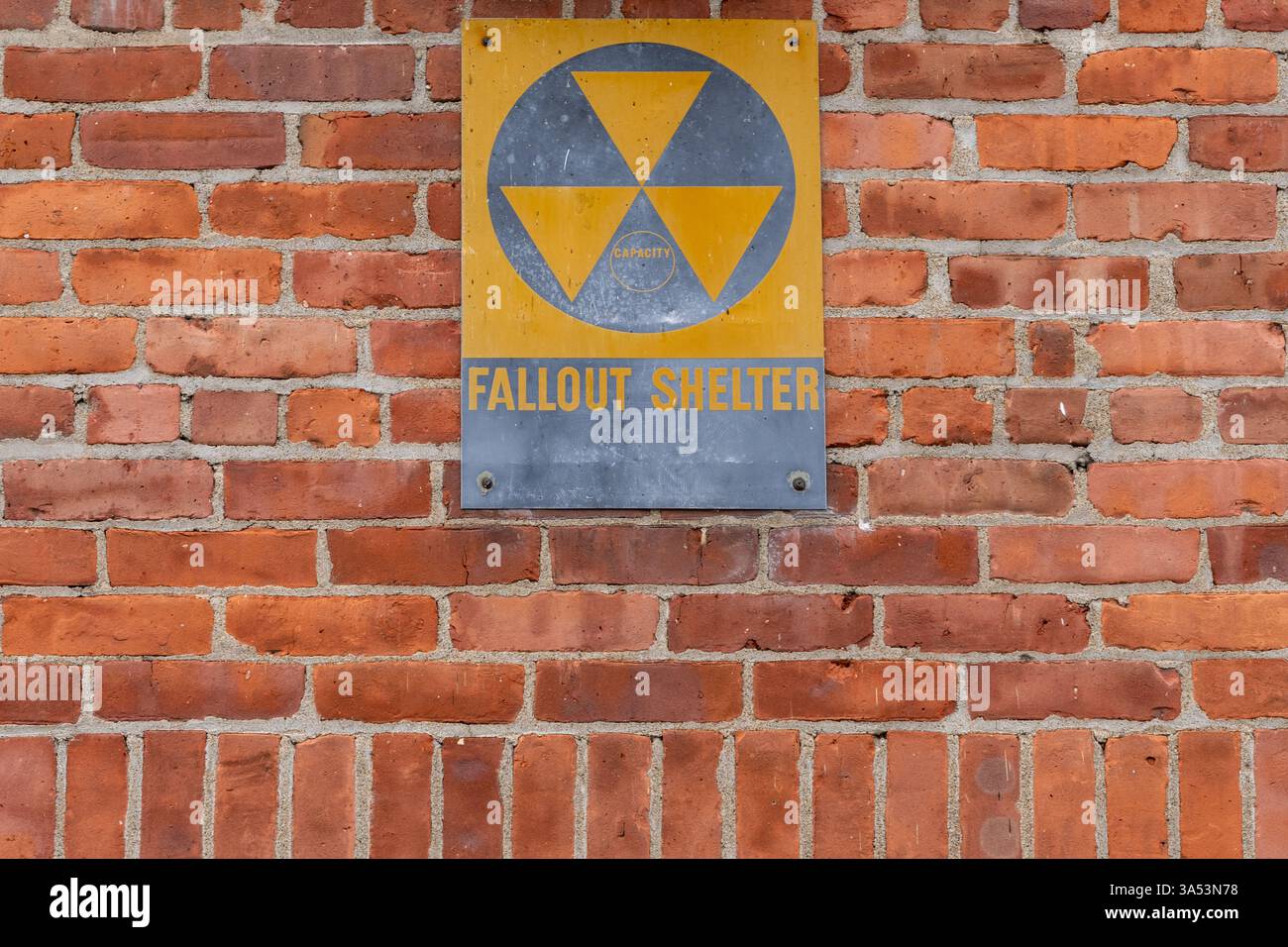 Ein altes gelbes silbernes Fallout-Schutzschild an der roten Ziegelwand Stockfoto