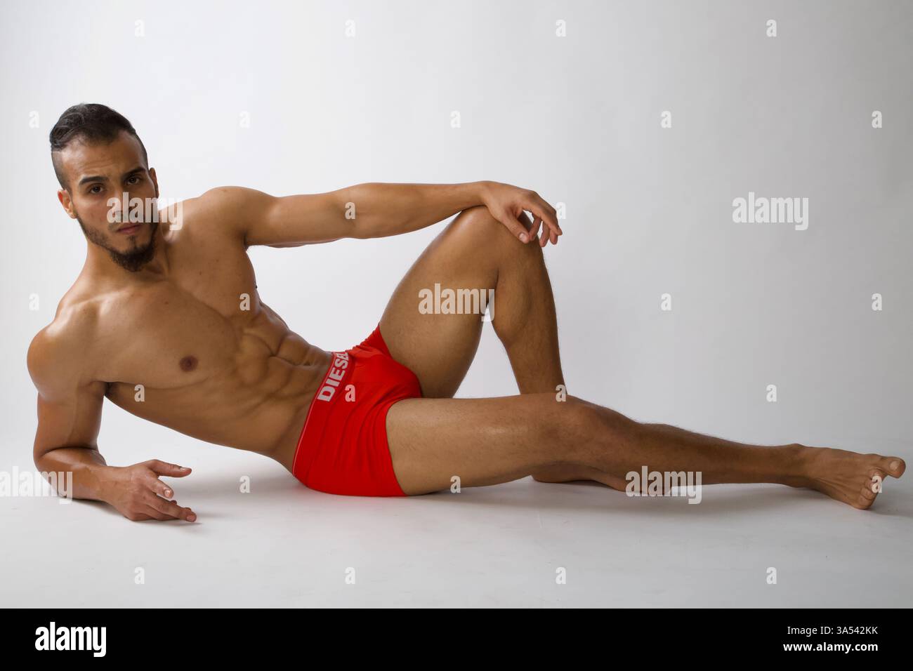 Männliches Model sitzt in entspannter Pose mit Hand am Knie Stockfoto