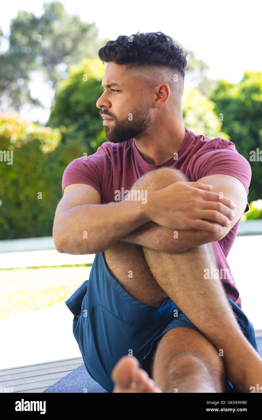 Mann, der sich draußen entspannt, im Kreuz auf Yogamatte sitzt und den sonnigen Tag genießt Stockfoto