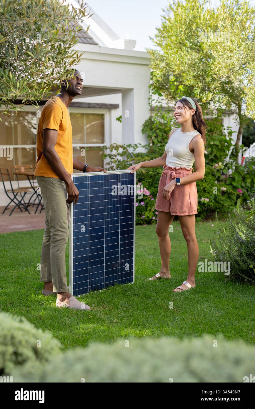 Diverse Paare genießen Urlaub, diskutieren über die Installation von Solarpaneelen in üppiger Gartenumgebung, Kopien Stockfoto