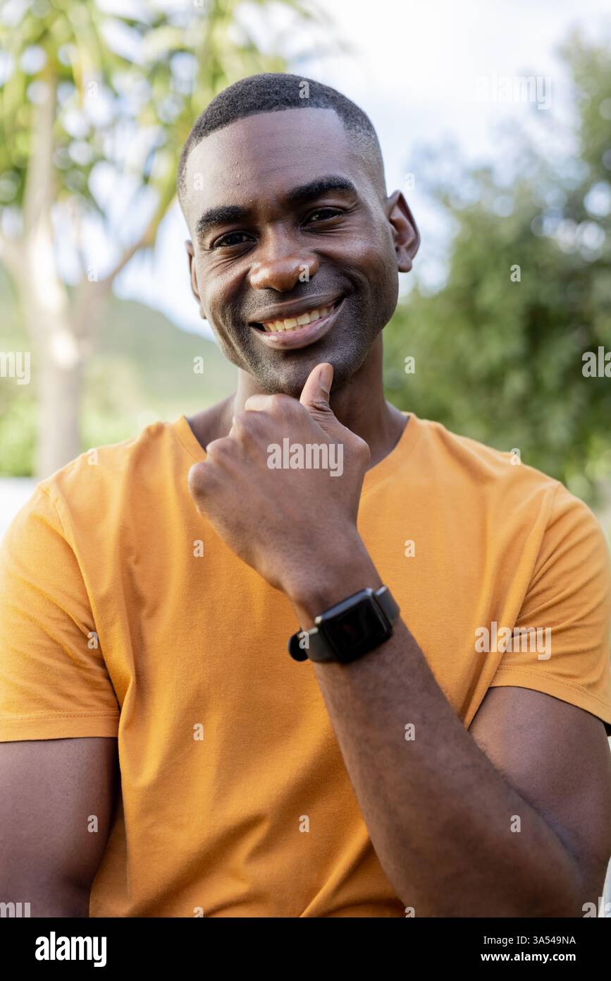 Lächelnder Mann in orangefarbenem Hemd genießt Outdoor-Urlaub, fühlt sich entspannt und glücklich Stockfoto