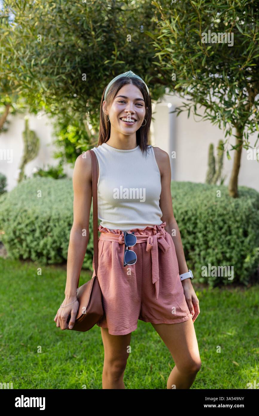 Lächelnde Frau im Garten in lässigem Outfit, genießt einen sonnigen Urlaubstag Stockfoto