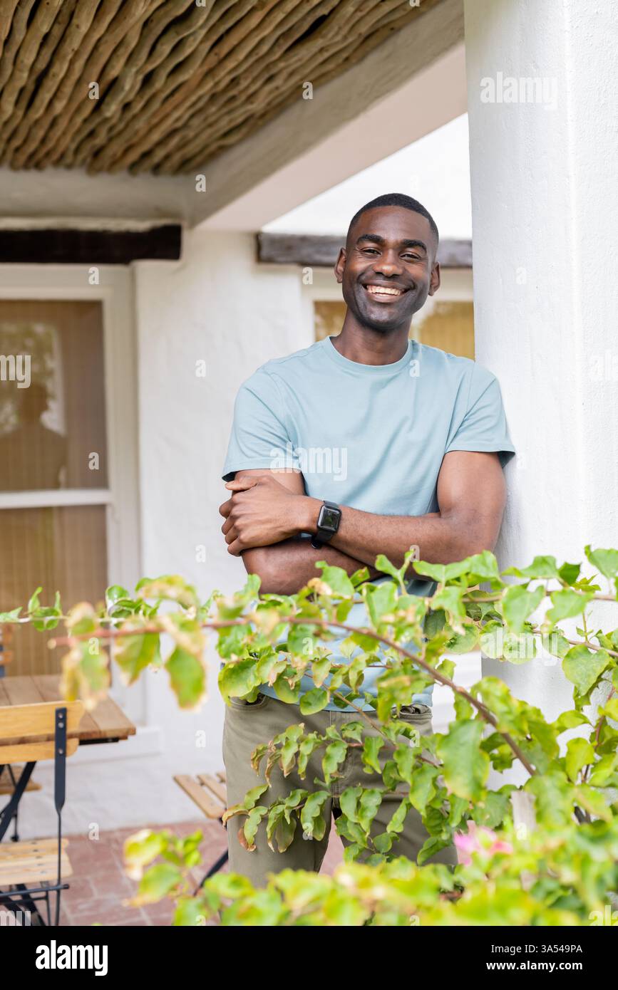 Lächelnder afroamerikanischer Mann, der sich auf der Veranda entspannt, Urlaub im Freien genießt Stockfoto