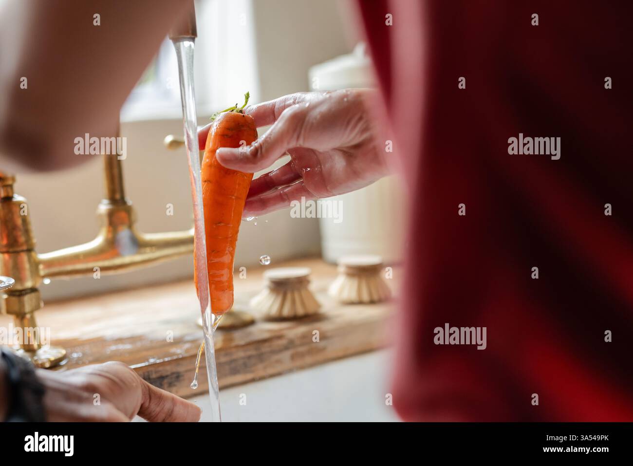 Frische Karotten unter fließendem Wasser in der Küche während des Ferienkochs waschen Stockfoto