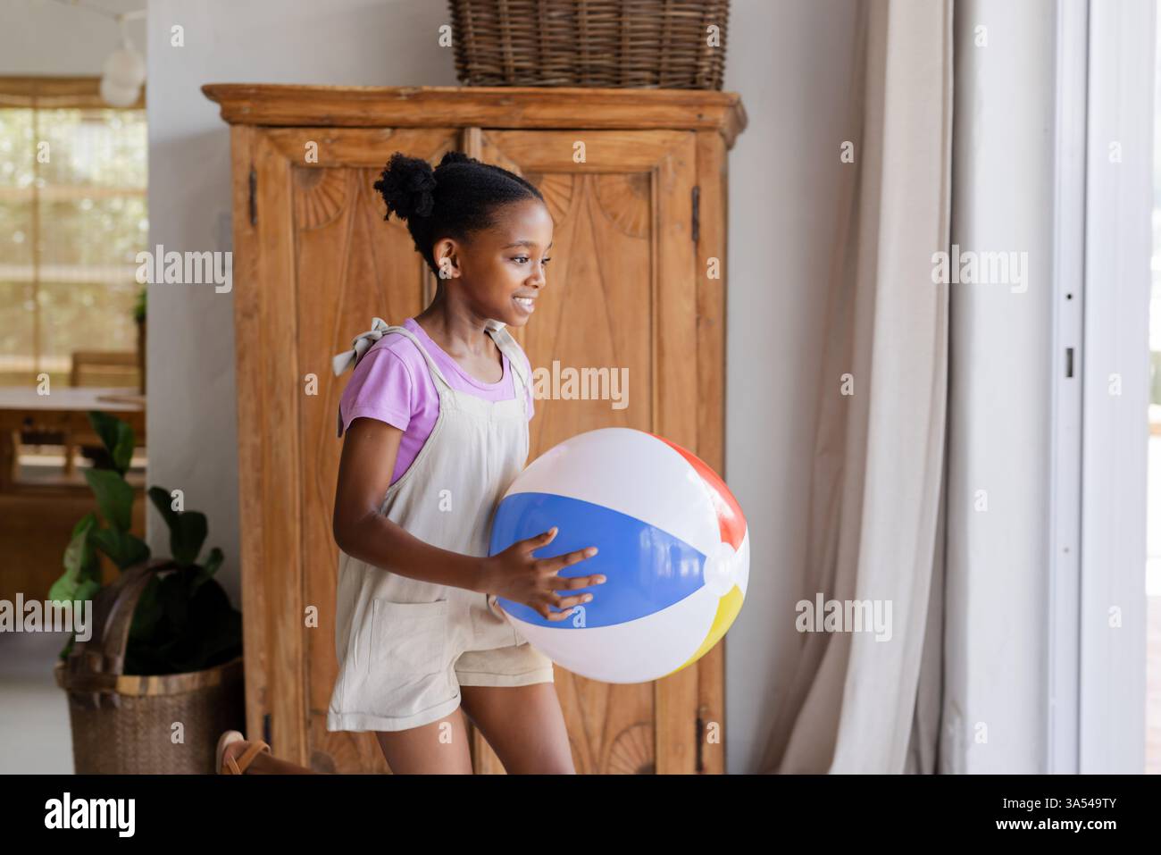 Junges Mädchen, das Strandball hält, lächelt und während des Familienurlaubs drinnen läuft Stockfoto