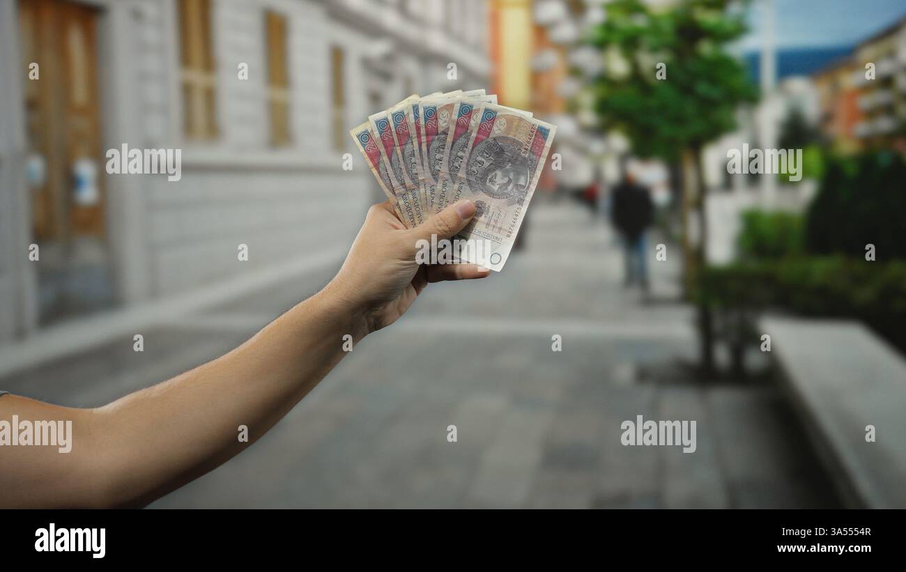 Ein Mann hält polnische Zloty-Banknoten in der Hand, steht draußen auf einer Stadtstraße und hebt Geld in einer städtischen Umgebung hervor. Stockfoto