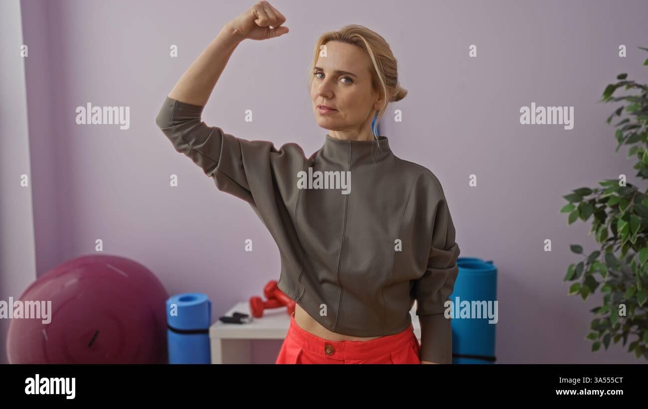 Frau beugt Arm im Fitnessstudio mit Trainingsball, zeigt Kraft und Fitness, in lässiger Trainingskleidung, in einem hell beleuchteten Sportzentrum mit Äquivalent Stockfoto
