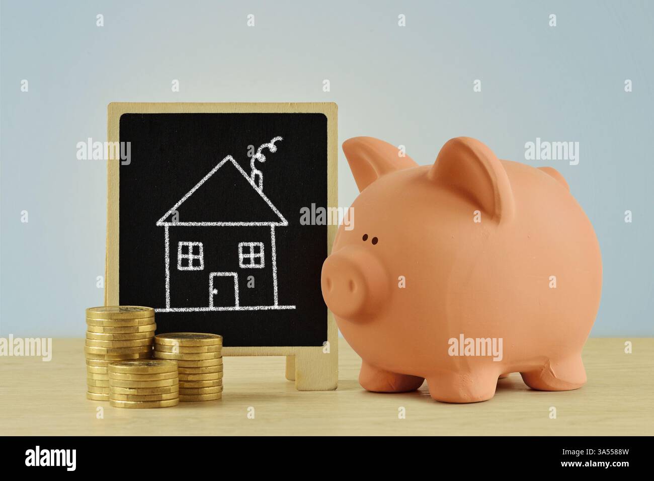 Schweinebank und Münzhaufen mit kindlichem Ziehhaus auf Tafel - Konzept des Sparens und Kaufhauses Stockfoto