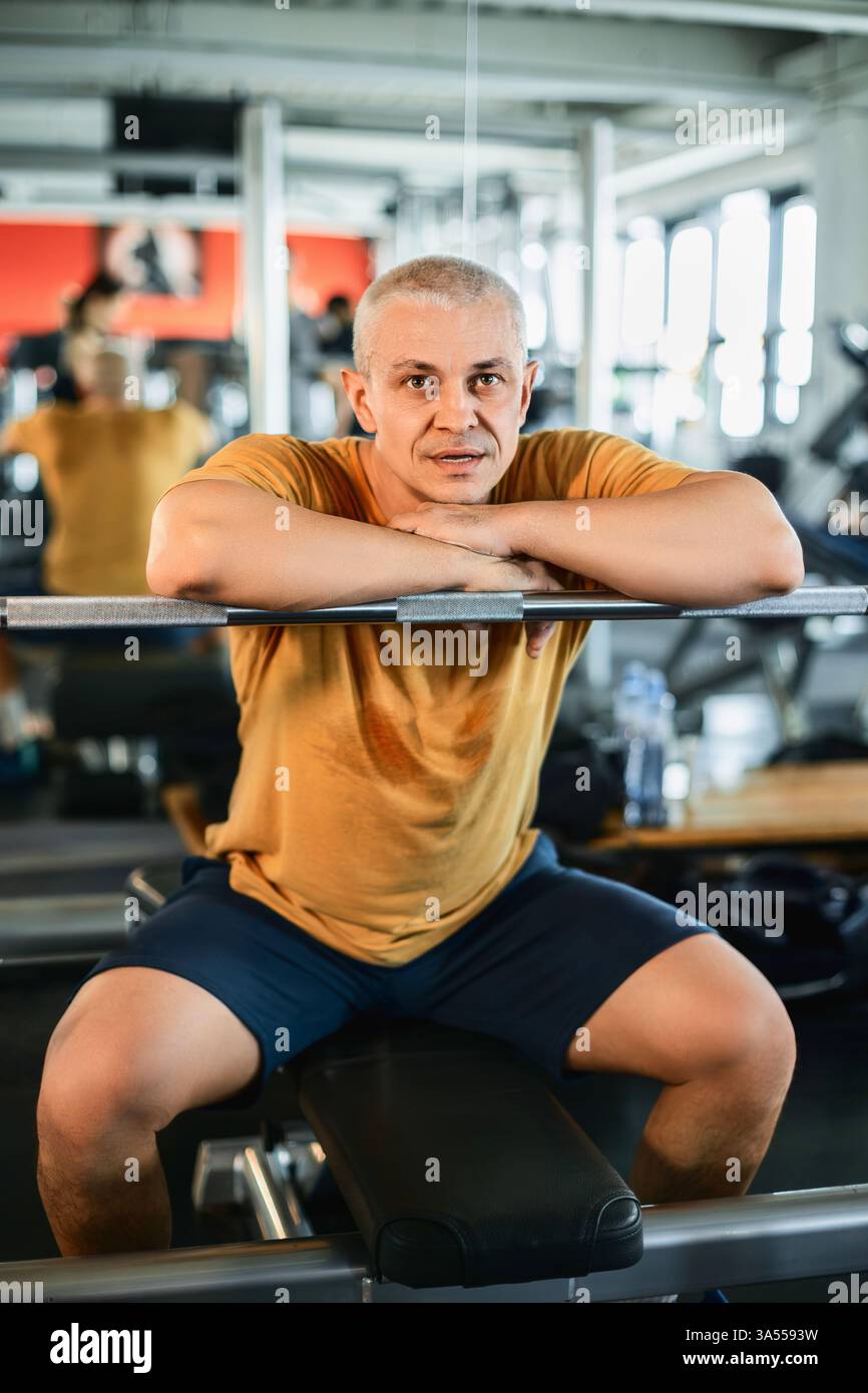 Athletischer Mann, der selbstbewusst auf der Langhantel in der Turnhalle ruht Stockfoto