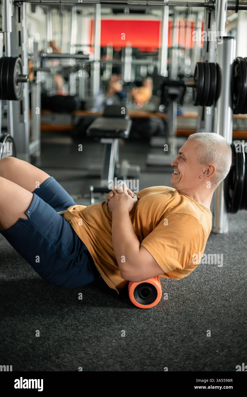 Mann, der Rückenmuskelregenerationsübungen mit einer Schaumwalze im Fitnessstudio macht Stockfoto