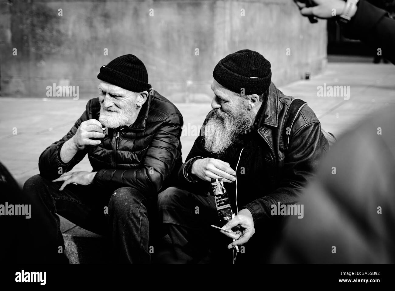Schwarz-weiß-Straßenfoto von zwei alten Männern mit Bärten und Hüten in Newcastle rauchend Stockfoto