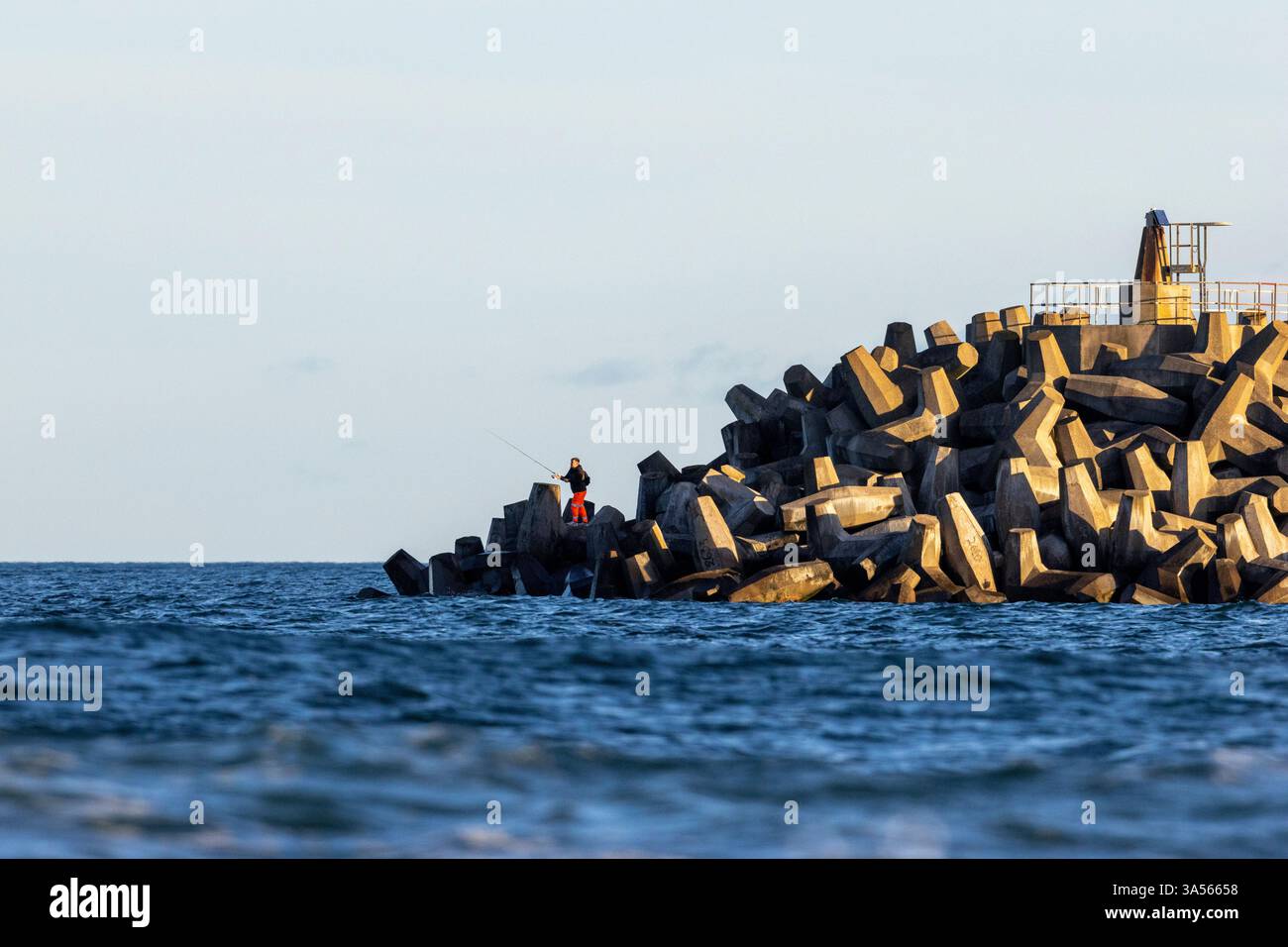 Der Mann stand beim Fischen zwischen den Dolos-Steinen des Kernkraftwerks Torness. East Lothian, Schottland, Großbritannien Stockfoto