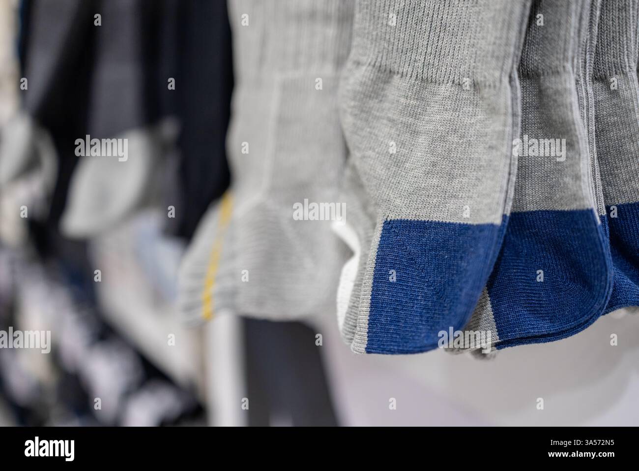 Graue und blaue Socken mit verstärkten Zehen- und Fersenpartien, die ordentlich auf einem Ladenregal angebracht sind und die weiche Strickstruktur und das strapazierfähige Material hervorheben Stockfoto