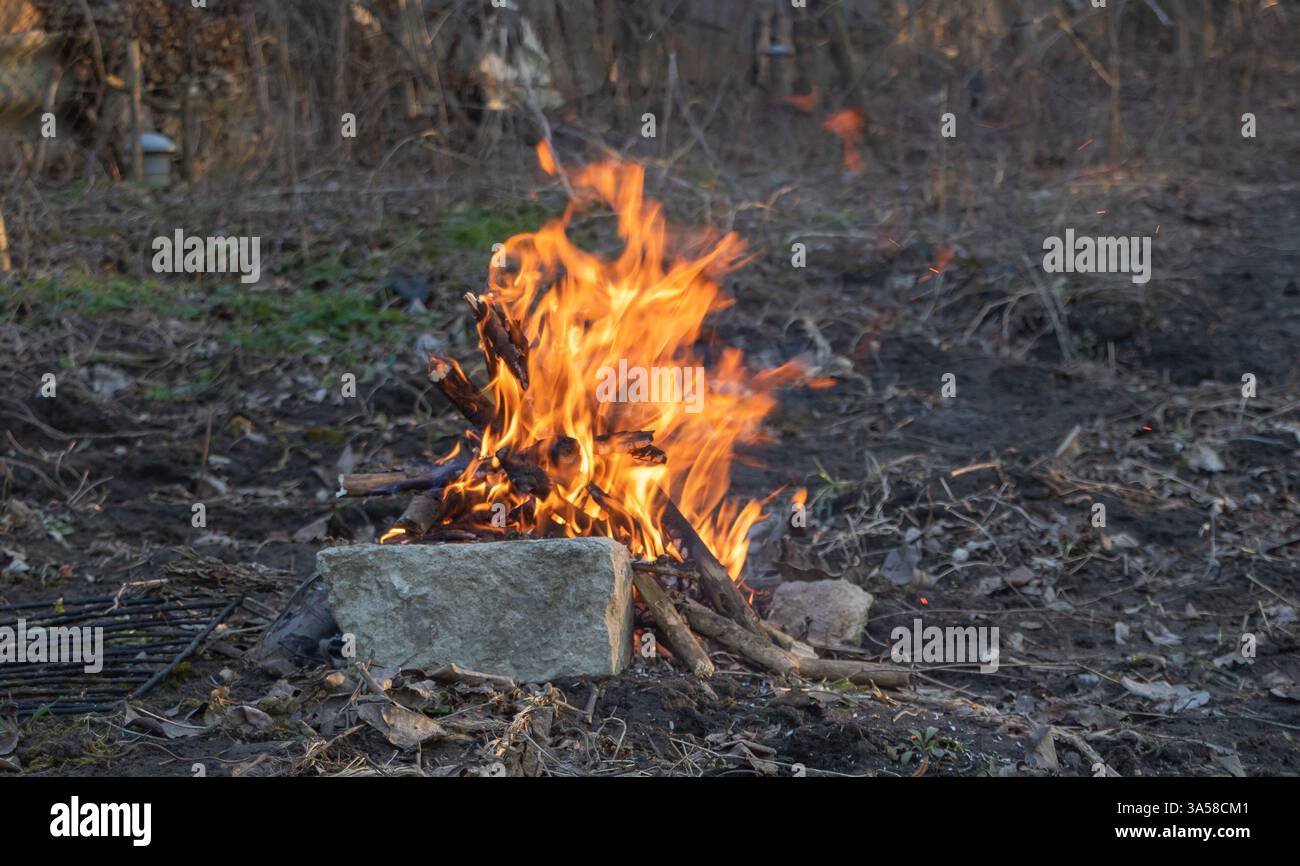 Ein kleines Feuer brennt im Wald in der Nähe einer alten Steinmauer. Die Abbildung zeigt eine Nahaufnahme der Flammen. Stockfoto