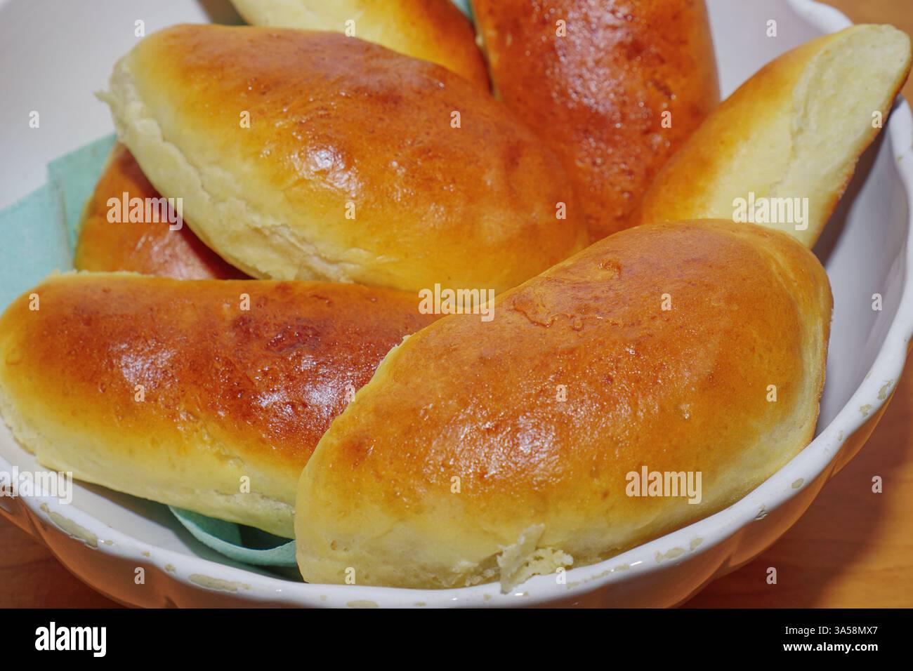 Frisch gebackene hausgemachte Kuchen mit goldbrauner Kruste in einer weißen Schüssel auf einem rustikalen Holztisch. Die warme, blättrige Textur und das reichhaltige Aroma vermitteln ein Gefühl von Wohnkomfort und traditionellem Backen. Konzept des hausgemachten Backens, traditionelle Küche, Komfortgerichte. Stockfoto