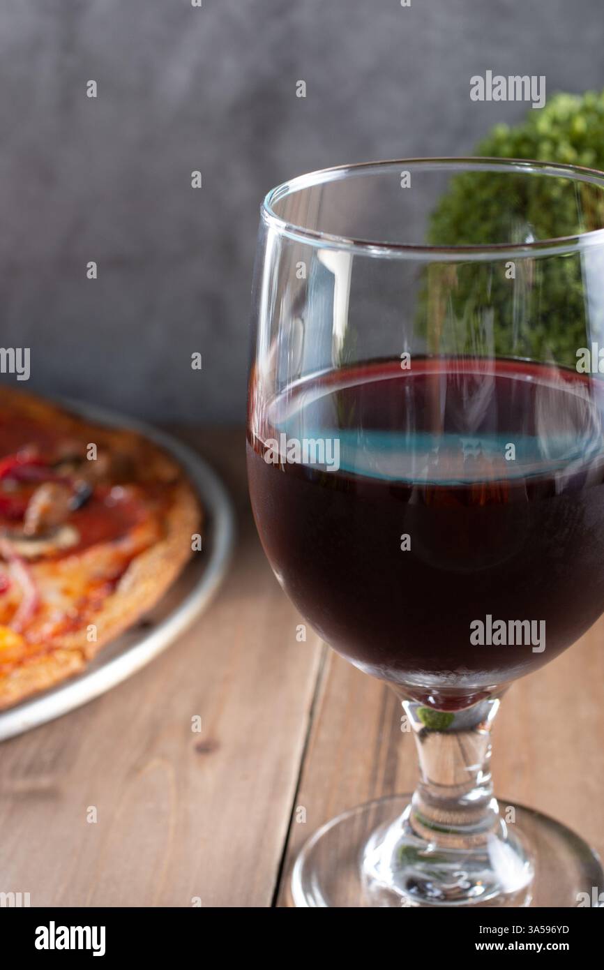 Ein Glas Rotwein aus der Nähe neben einem Pizzakuchen. Stockfoto