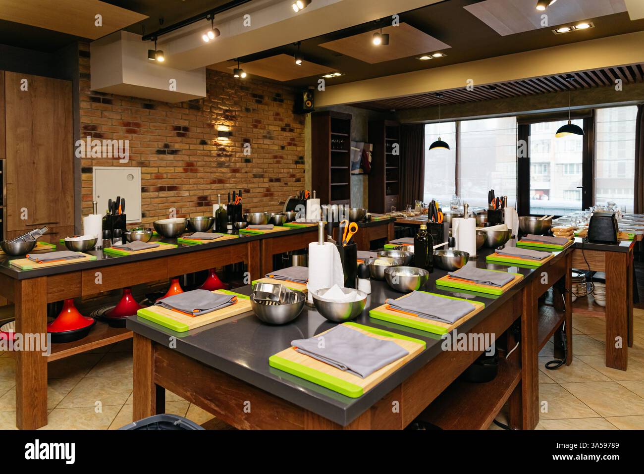 Eine geräumige Küche für Kochkurse mit mehreren Arbeitsplätzen, die jeweils mit Schneidebrettern, Messern, Schüsseln und Utensilien ausgestattet sind, bereit für einen kulinarischen Genuss Stockfoto