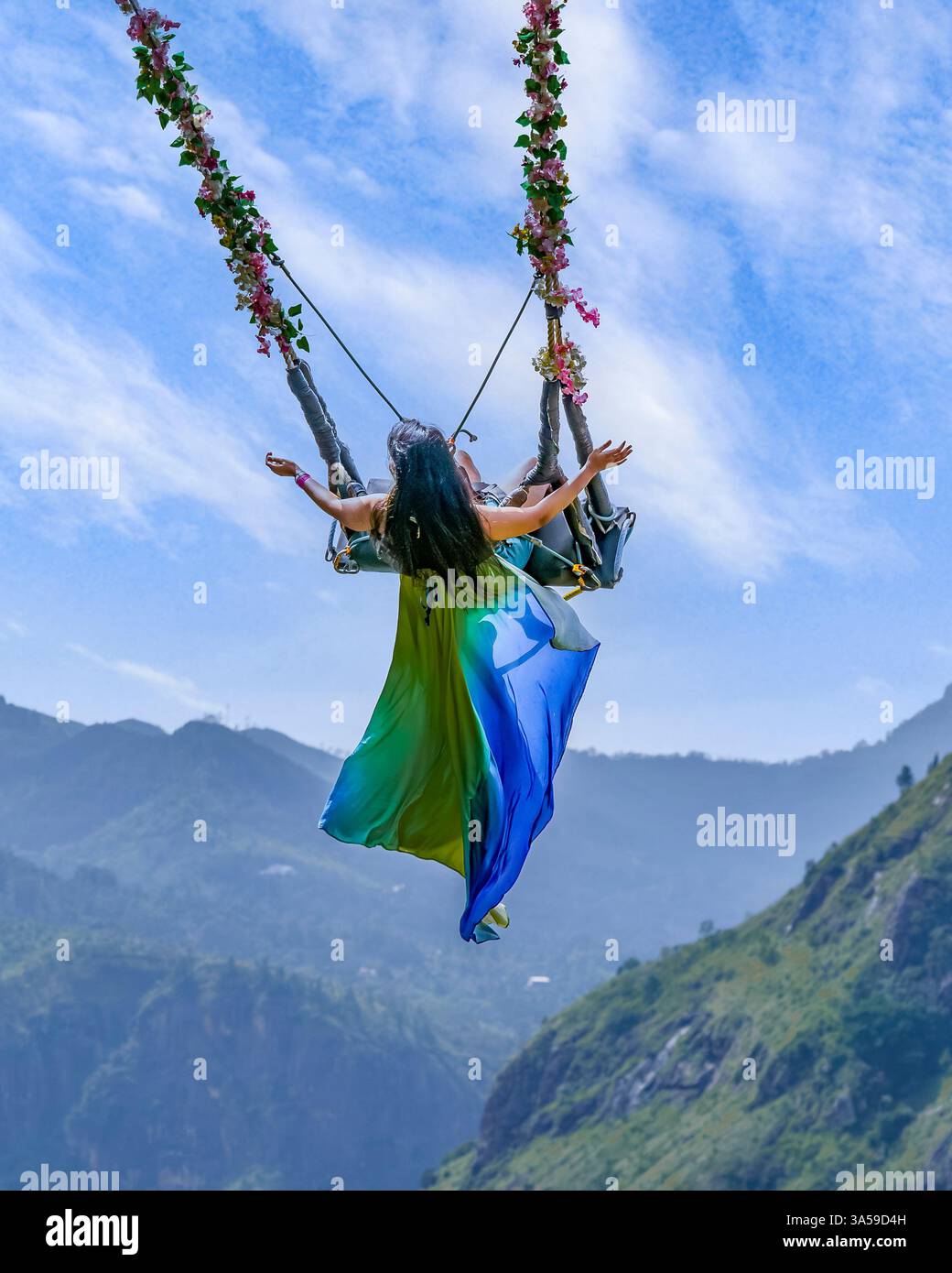 Eine Frau schwingt hoch über den üppigen Hügeln von Ella, Sri Lanka, mit Little Adam's Peak im Hintergrund und genießt ein aufregendes und landschaftlich reizvolles Abenteuer in n Stockfoto