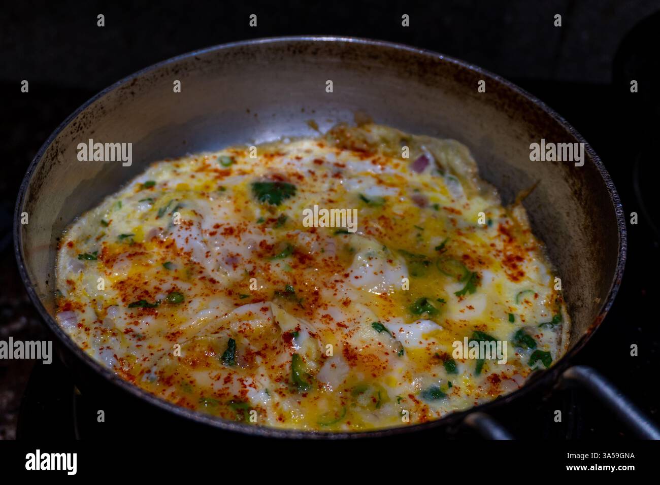 Gemischtes Gewürzomelette mit grüner Garnitur auf einem Kochfeld in einer indischen Küche, kulinarische Köstlichkeiten. Stockfoto