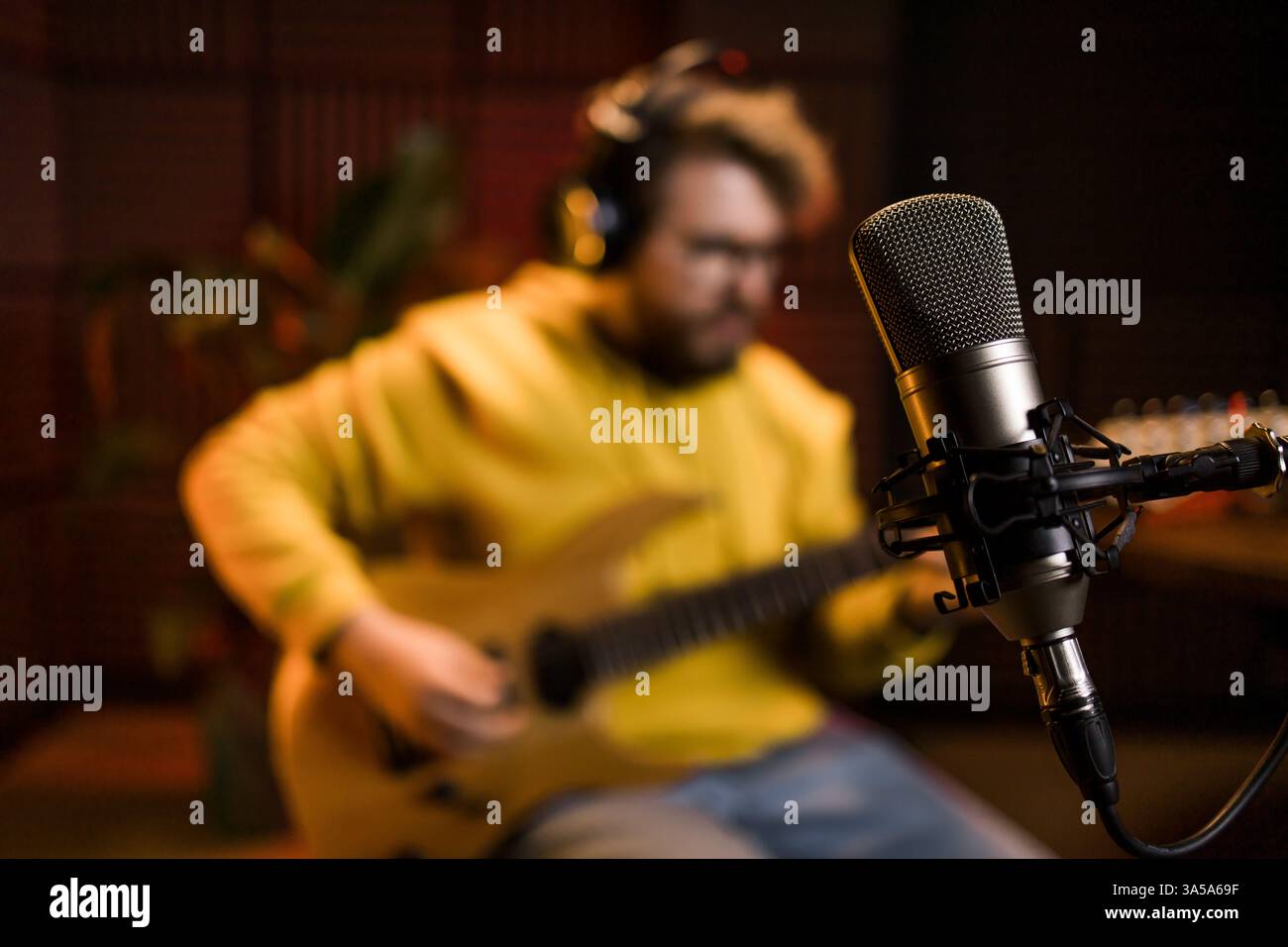 Ein fokussierter männlicher Musiker stimmt eine Bassgitarre vor dem Hintergrund einer digitalen Klangbearbeitung in einer modernen Studio-Umgebung ab Stockfoto