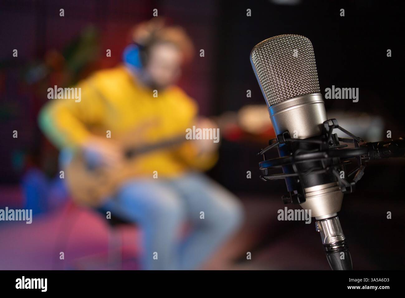 Ein fokussierter männlicher Musiker stimmt eine Bassgitarre vor dem Hintergrund einer digitalen Klangbearbeitung in einer modernen Studio-Umgebung ab Stockfoto