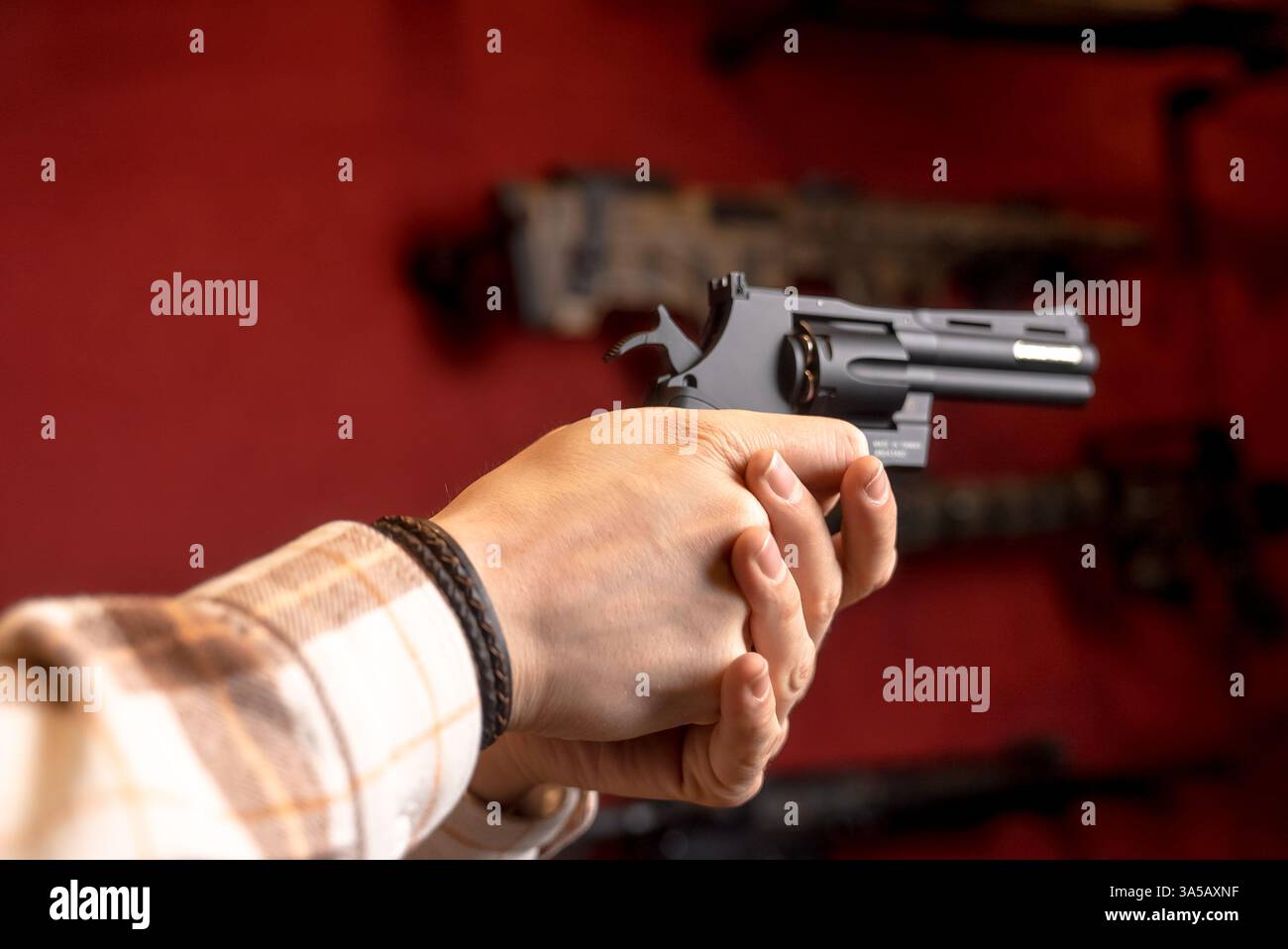 Ein Mann hält einen Black Revolver mit beiden Händen in einem Waffenladen. Nahaufnahme auf rotem Hintergrund Stockfoto