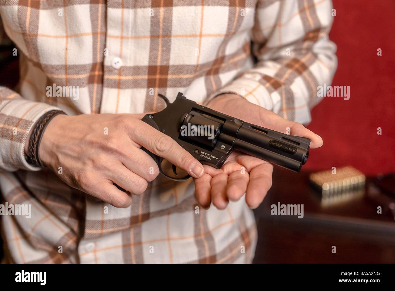 Ein Mann hält einen Black Revolver mit beiden Händen in einem Waffenladen. Nahaufnahme auf rotem Hintergrund Stockfoto