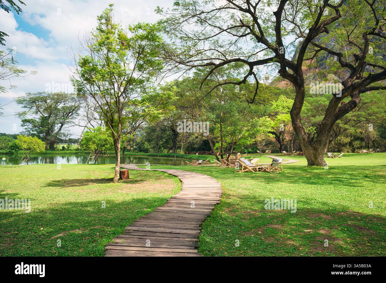 Ein ruhiger Holzweg lädt Besucher ein, eine üppige grüne Landschaft neben einem ruhigen Gewässer zu erkunden, perfekt zum Entspannen und Genießen der Natur Stockfoto