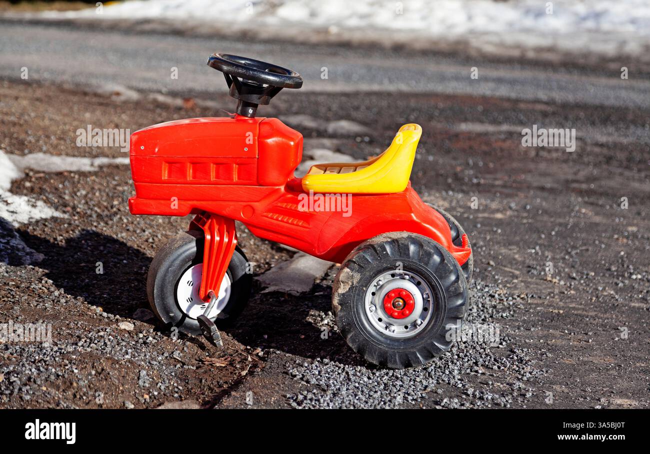 Ein leuchtend roter Spielzeugtraktor sitzt auf Kies und fängt die Essenz des Spiels und der Fantasie der Kindheit ein. Der auffällige Kontrast zwischen dem hellen Stockfoto