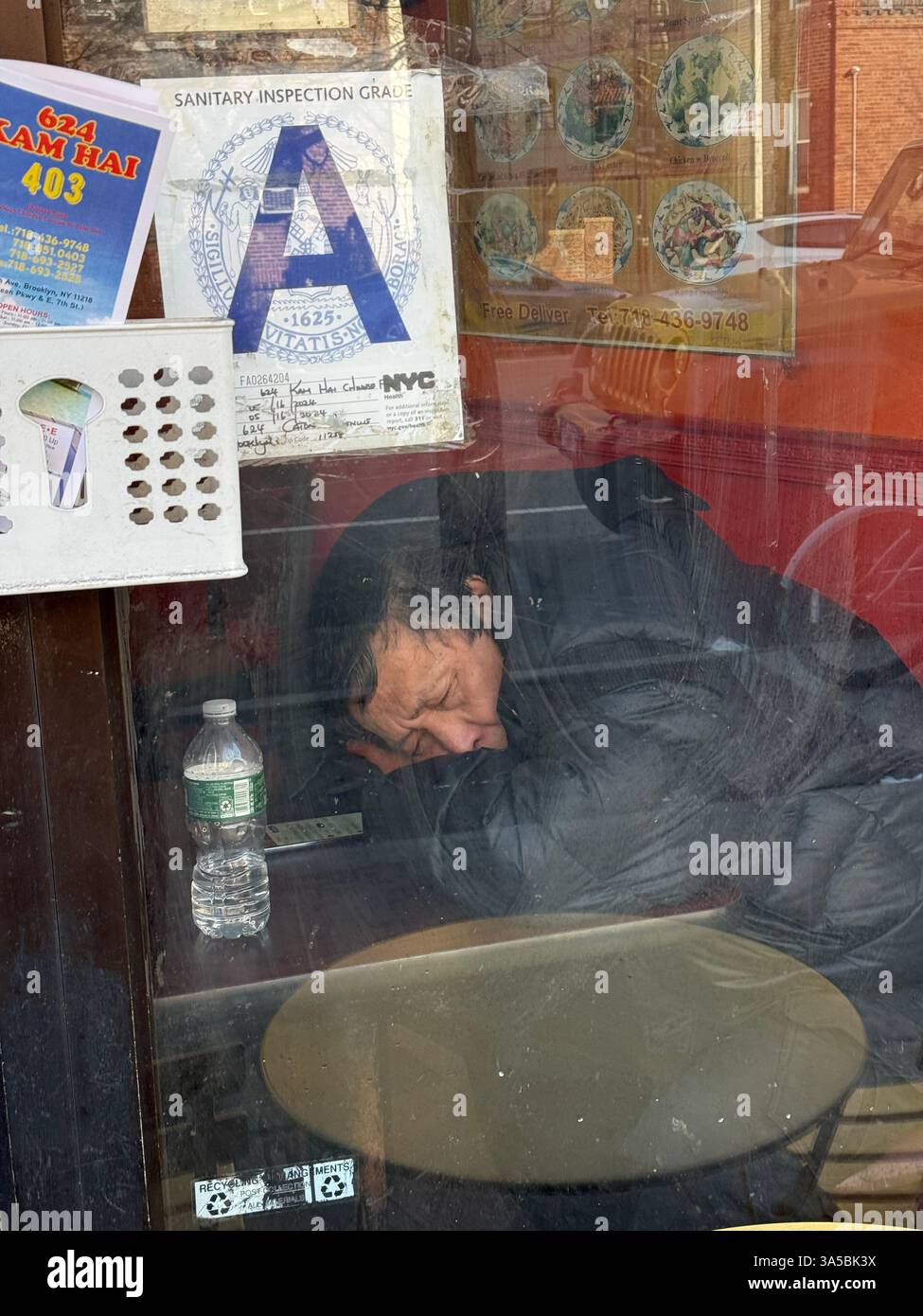 Durch das Fenster auf einen müden Lieferarbeiter in einem chinesischen Restaurant in Brooklyn, New York. Stockfoto