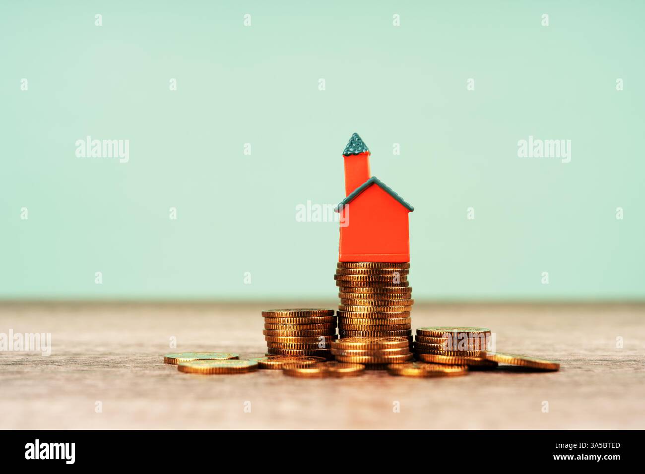 Miniaturhaus auf dem grünen Hintergrund des Münzstapels Stockfoto