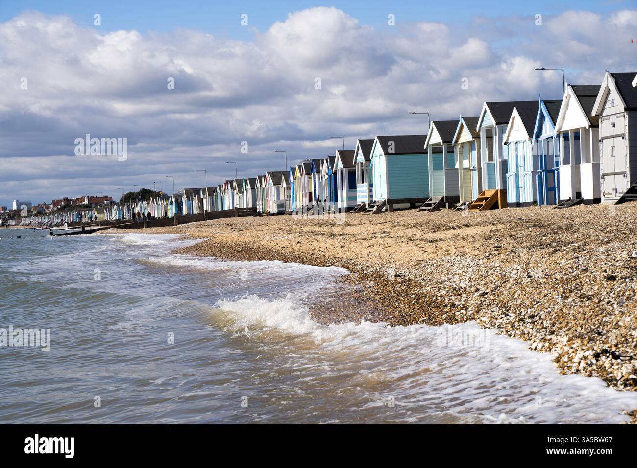 Blick auf eine Reihe von Strandhütten entlang der Küste von Southend-on-Sea am sonnigen Frühlingstag, Wasserwellen brechen am kopfsteingepflasterten Strand Essex England Großbritannien Stockfoto