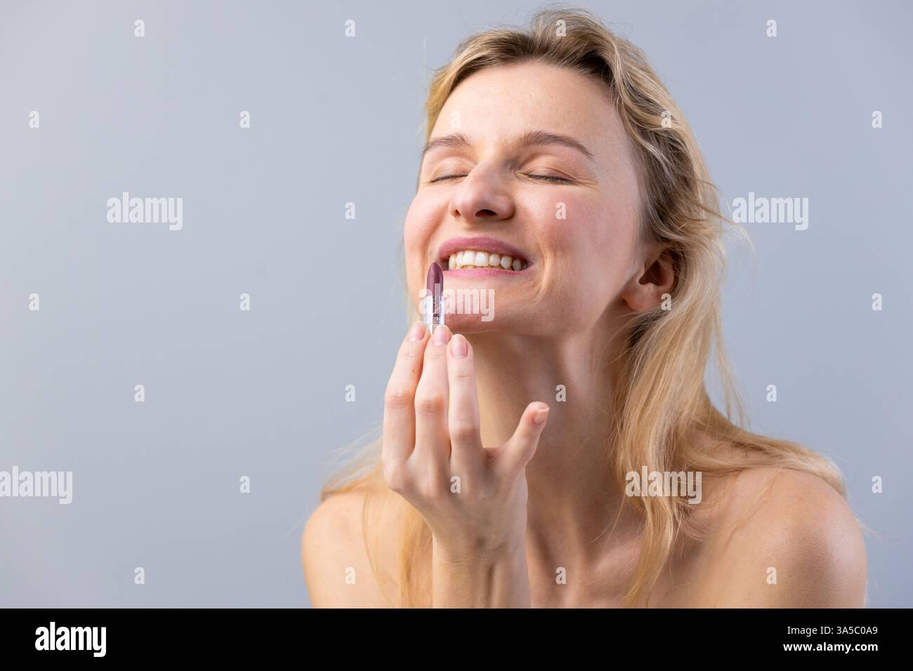 Ein freudiger Moment: Frau trägt Lippenstift mit einem Lächeln auf, nimmt Schönheit und Selbstvertrauen in einer ruhigen Umgebung auf und hebt Selbstpflege und Persönlichkeit hervor Stockfoto