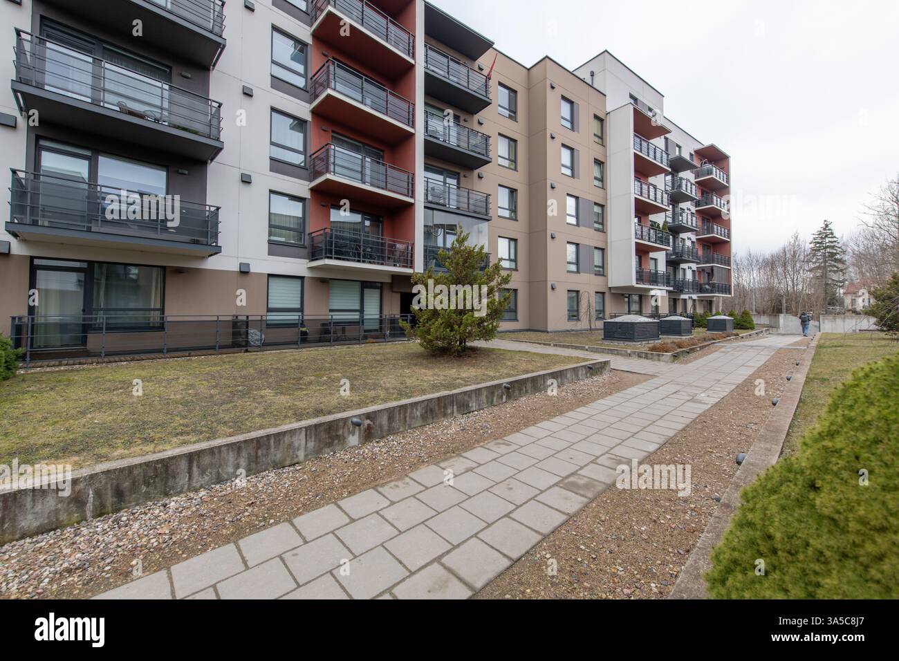 Modernes Wohngebäude mit mehrstöckigen Balkonen, landschaftlich gestaltetem Grün und einem gepflasterten Fußgängerweg in einem Vorstadtviertel an einem cl Stockfoto