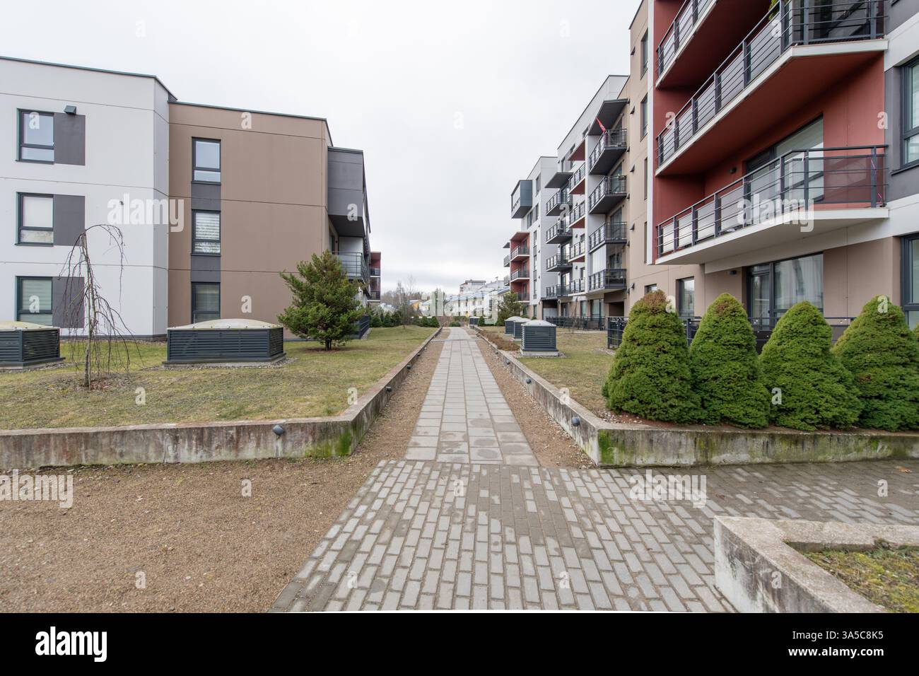 Modernes Wohngebäude mit mehrstöckigen Balkonen, landschaftlich gestaltetem Grün und einem gepflasterten Fußgängerweg in einem Vorstadtviertel an einem cl Stockfoto