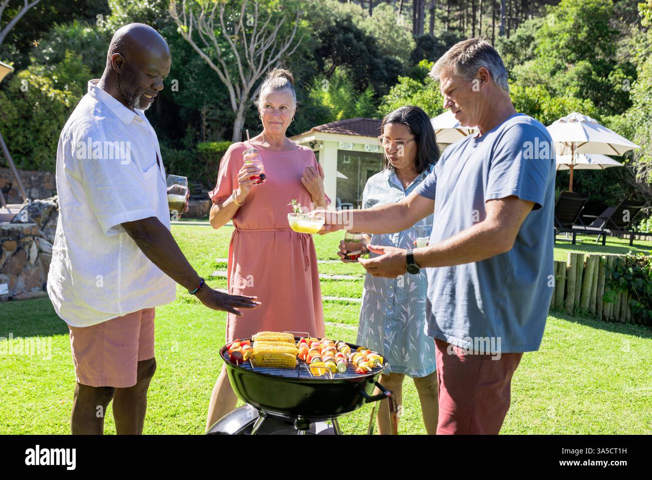 Senioren-Freunde genießen Barbecue im Freien und servieren Speisen und Getränke im sonnigen Hinterhof Stockfoto