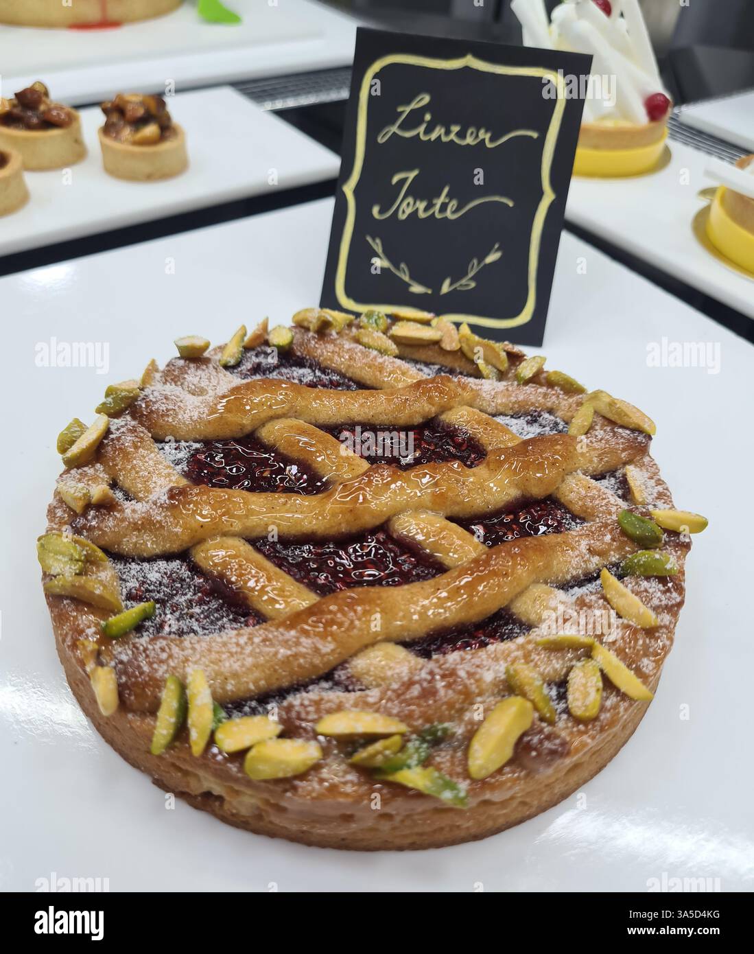Eine wunderschön dekorierte Linzer-Torte mit Gitterkruste, Himbeermarmelade und mit Puderzucker und Pistazien bestreut, die auf einem Witz präsentiert werden Stockfoto