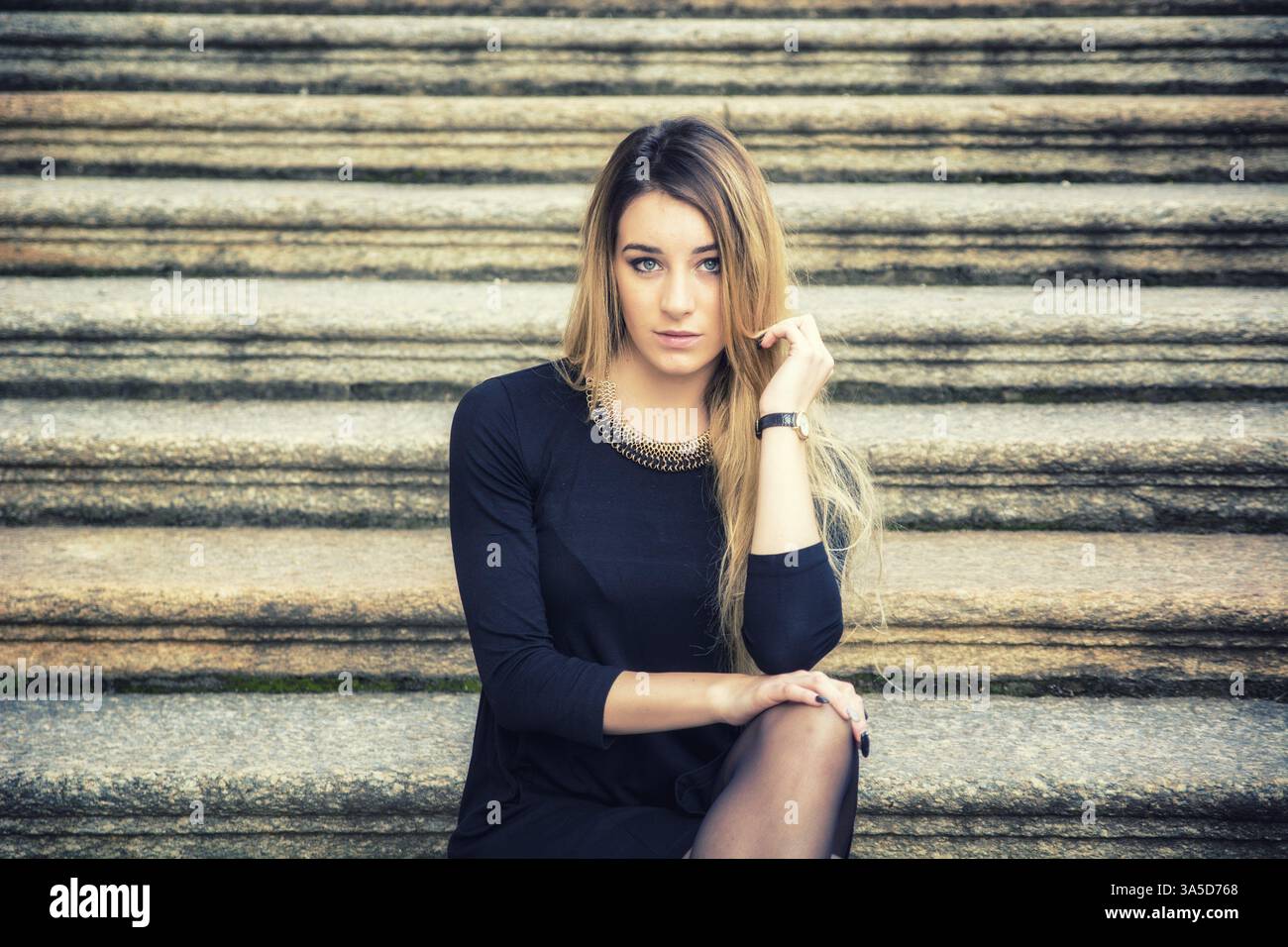Porträt von attraktive blonde junge Frau im schwarzen Kleid, im freien Blick in die Kamera, auf großen alten Steintreppen Stockfoto