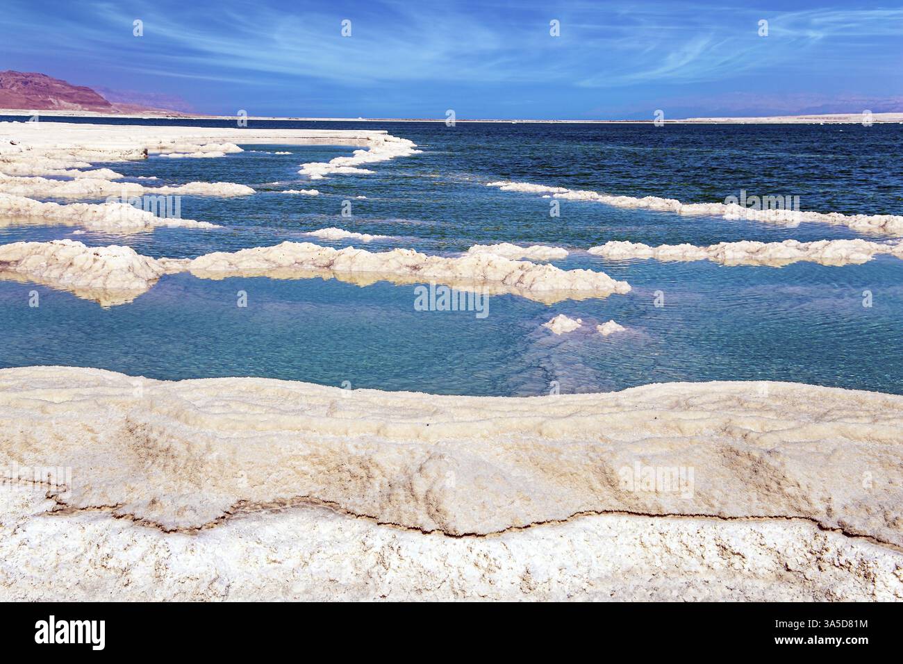 Das verdampfte Salz bildet bizarre Muster auf der Wasseroberfläche. Zirrus Wolken fliegen am blauen Himmel. Windiger Frühlingstag. Die israelische Küste der Stockfoto