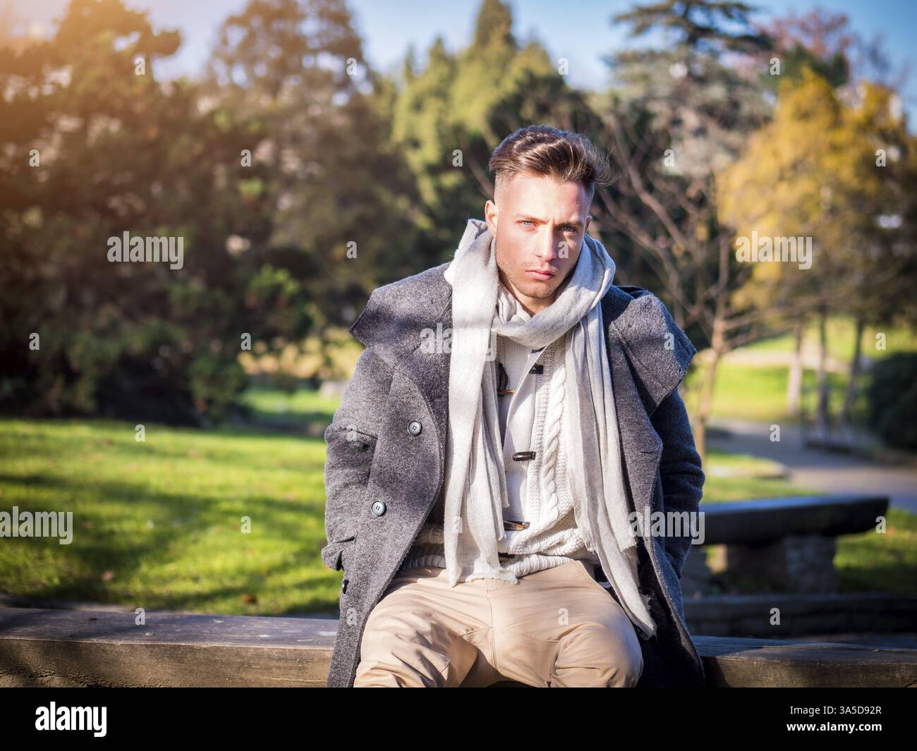 Schöne moderne, junge Mann, sitzend im City Park trägt einen modischen Pullover oder Jacke und Schal Stockfoto