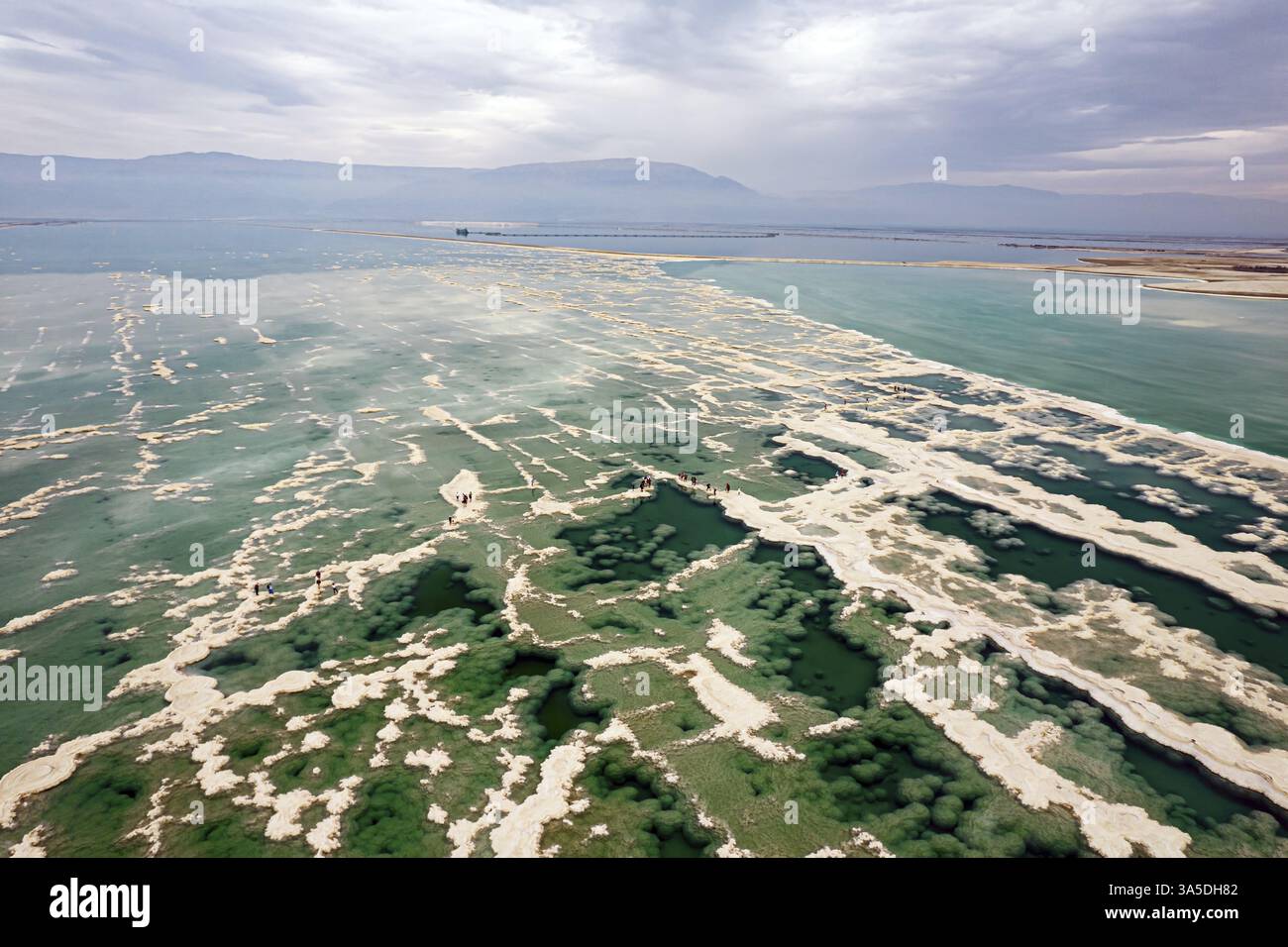 Türkisfarbenes Wasser und weiße Salzflecken. Das aus dem Wasser verdampfte Salz bildet bizarre Muster im flachen Meerwasser. Bewölkter Winterhimmel. Drohne Photogr Stockfoto