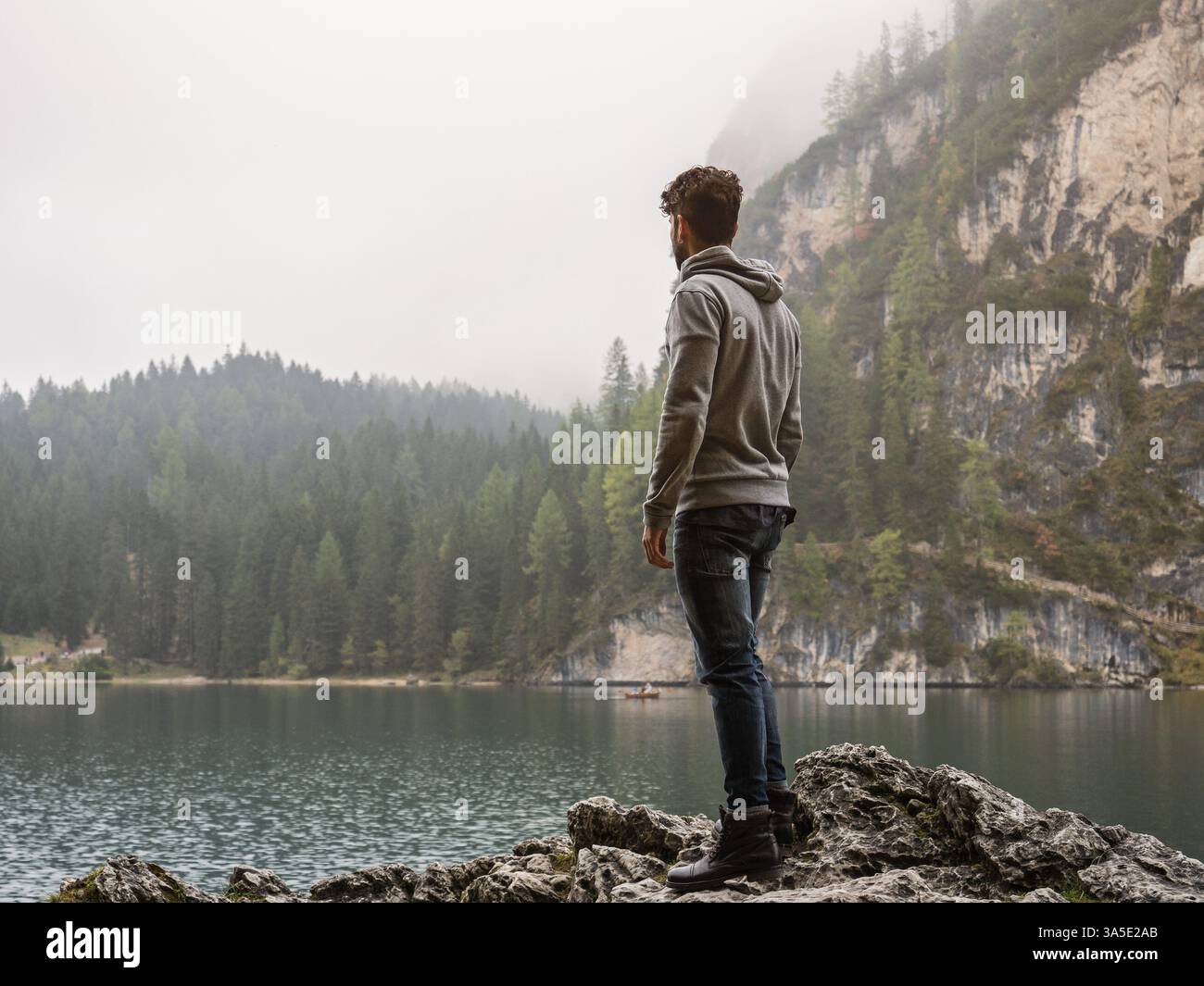 Schöner Yung-Mann, der auf dem Hintergrund des Waldes am Ufer des Sees steht und wegblickt Stockfoto