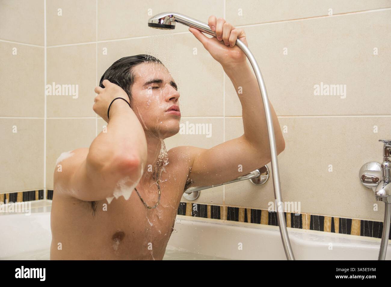 Hübscher junger Mann in Badewanne haben zu Hause Bad, Körper und Haare mit Bathfoam und Shampoo waschen Stockfoto