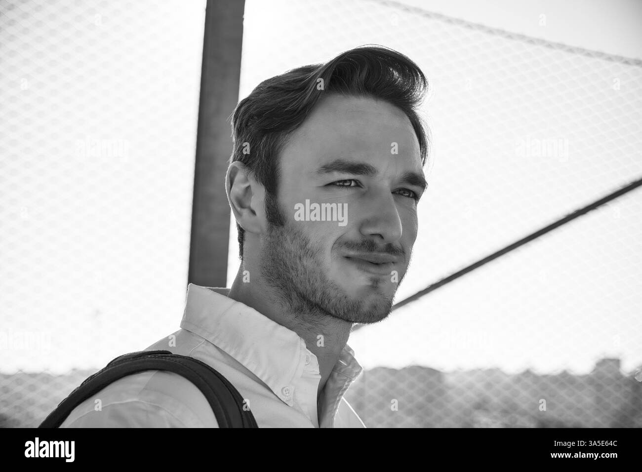 Hübscher junger Mann zu Fuß in die Stadt mit Rucksack auf der Schulter, trägt weißes Hemd, Blick in die Kamera Stockfoto