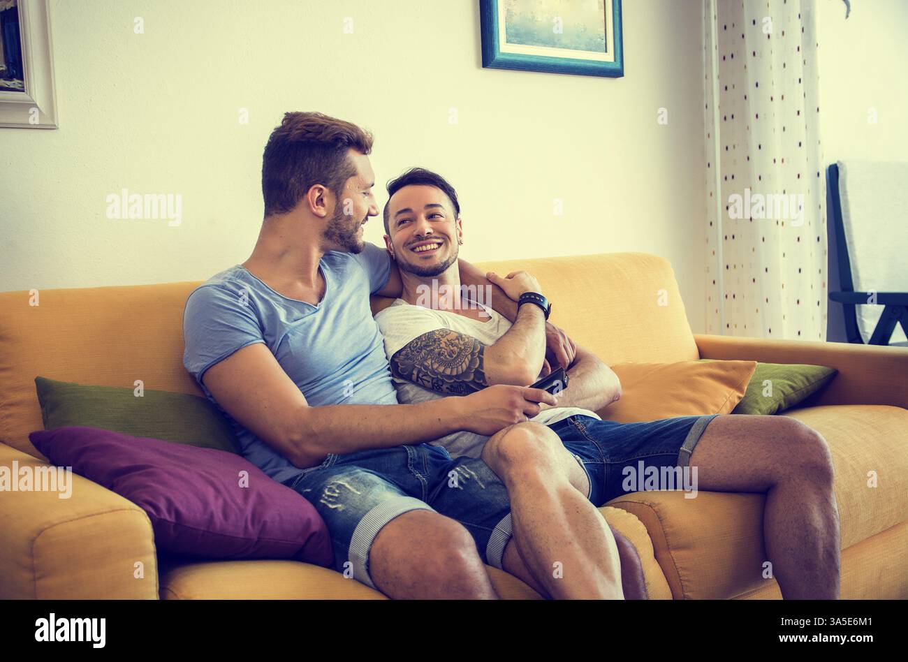 Zwei homosexuelle Männer in casual Outfits sitzen auf dem Sofa und Fernsehen zu Hause Stockfoto