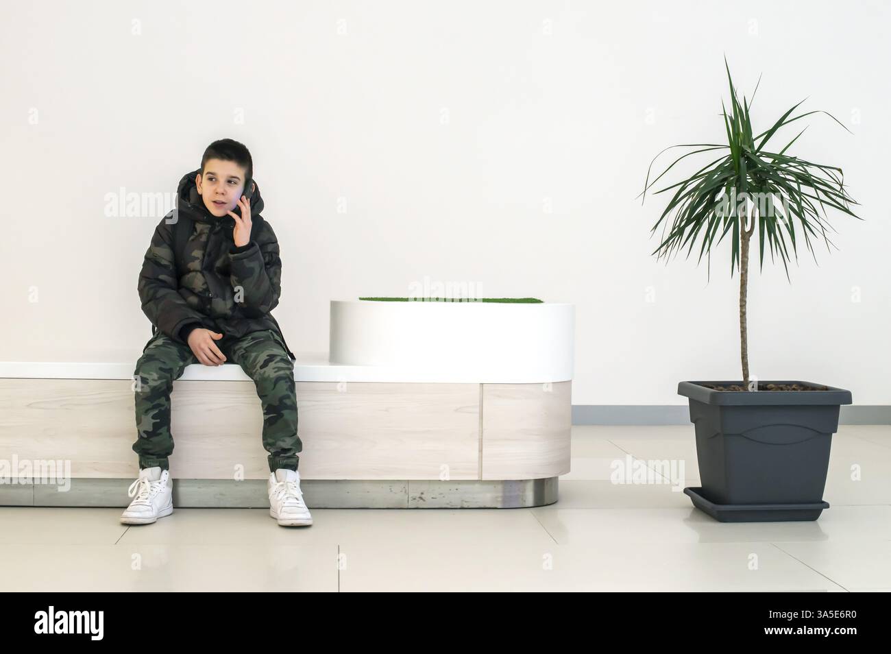 Teenager sprechen auf dem Smartphone in der modernen kommerziellen Zentrum. Sitzbank und Blume in einem Topf. Modernes Gebäude. Technologie- und Kommunikationskonzept Stockfoto